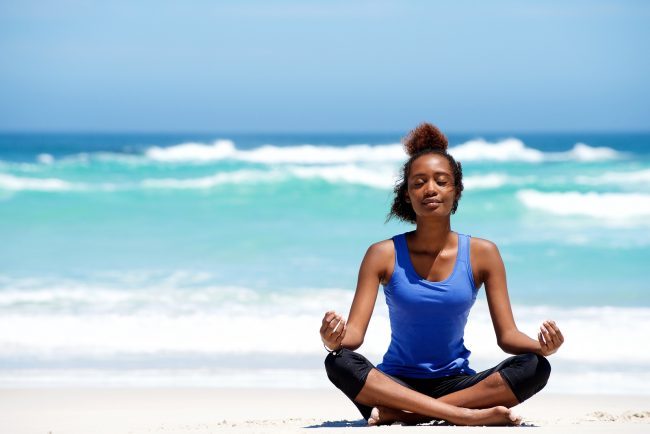 Portrait of young african american woman meditating in yoga pose outdoors at the beach